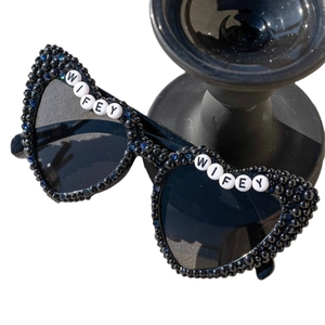 Black heart-shaped WIFEY sunglasses with pearl beads and rhinestones on white background