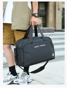 Outdoor view of a black high-capacity travel bag with Happy Travel print and shoulder strap