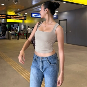 Outdoor shot of a woman in a beige square neck crop top and blue denim jeans