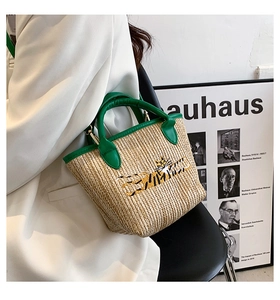 Detail of straw woven tote bag featuring green handles and tiger embroidery on khaki base