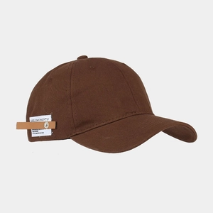 Close-up of brown cotton baseball cap side detail with white woven label and leather strap