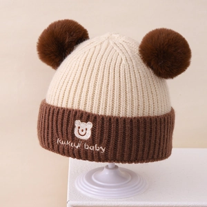 Detail der Kinder-Strickmütze mit doppelten Pompons und süßer Bären-Stickerei-Design