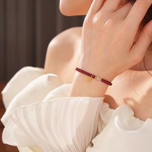 Close-up of cinnabar bead bracelet with white jade bead and gold pendant on wrist