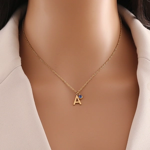 Détail d'un collier doré avec pendentif lettre A et perle bleue sur un mannequin en blanc