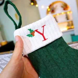 Green knitted Christmas stocking with white cuff and red embroidered letter Y and holly