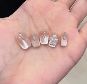 Detailed view of pink cat-eye gradient press-on nails with 3D white flowers and rhinestones