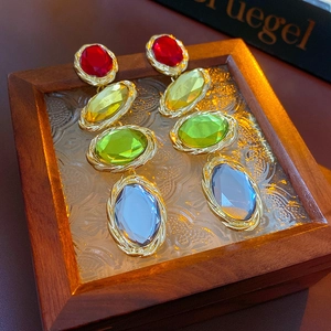 Close-up of vintage gold earrings with colorful oval stones on textured glass box