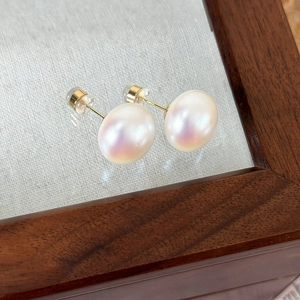 Close-up of pink lustrous pearl studs on a vintage wooden jewelry box with golden posts