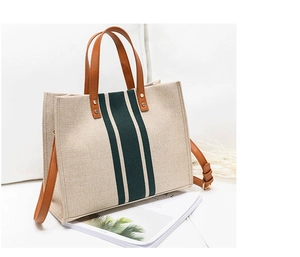 Detail view of cream canvas tote bag with green stripes and brown leather handles