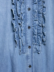 Close-up of light blue denim shirt featuring ruffled lapels and dark circular buttons
