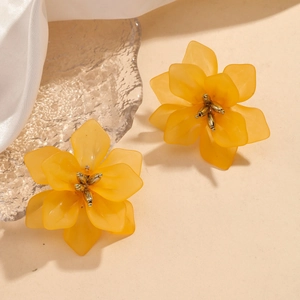 Chic yellow acrylic floral stud earrings with golden pistils on a textured beige surface