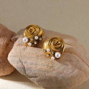 Detail of snail shell design gold earrings with pearls and rhinestones on stone background