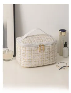 Detail of tweed makeup bag featuring gold double zippers and a white leather handle