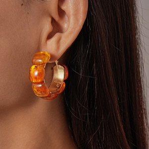 Close-up of amber resin C-shape hoop earrings with gold metal base on model