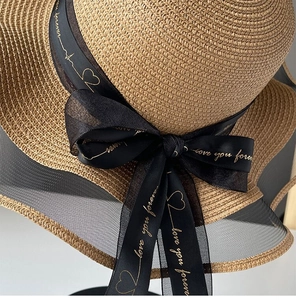 Detail view of woven straw sun hat texture with black chiffon bow and mesh brim