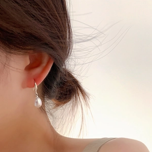 Macro view of white teardrop pearl earrings with silver hooks on ear model