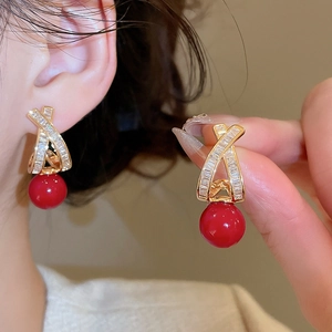 Detail of cross earrings with gold plating, cubic zirconia, and red sphere drops