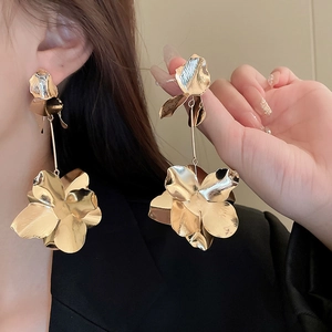 Close-up of golden oversized metal flower earrings with long fringe tassels