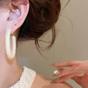Detail of minimalist cream velvet flocked hoop earrings worn by a model in warm light