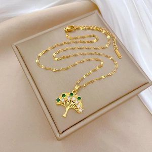 Detailed view of golden Tree of Life pendant with green crystals on silk background
