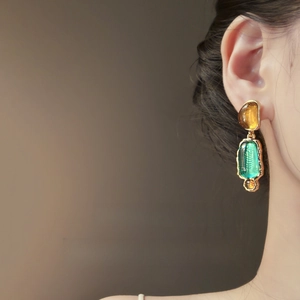 Vintage style gold earrings featuring amber and green resin geometric pendants on a model