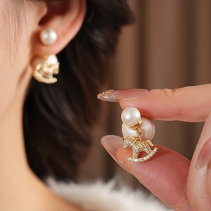 Macro detail of gold rocking horse earring featuring white zircon pavé and large pearl charm