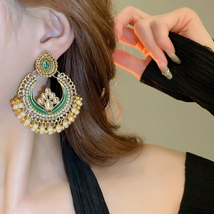 Detailed side view of ethnic gold and green drop earrings with white pearl tassels
