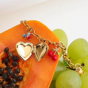 Gold cherry and heart charms on a delicate chain necklace styled with fresh fruits