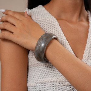 Primo piano di un ampio bracciale in resina con motivo marmorizzato grigio al polso