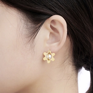 Elegant gold flower earrings with central pearl shown on a model with soft lighting