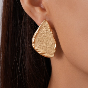 Detail of a hammered irregular golden geometric stud earring worn on a model ear