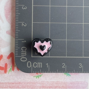 Macro view of a 1cm mini black resin heart charm with pink inlay on a scale ruler