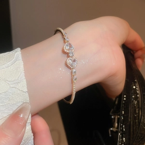 Detail of model wearing a gold zircon heart bracelet with sparkling clear crystals