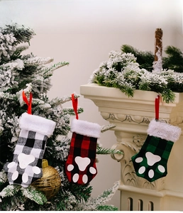 Close-up of buffalo plaid pet paw stockings hanging on a white mantel and Christmas tree