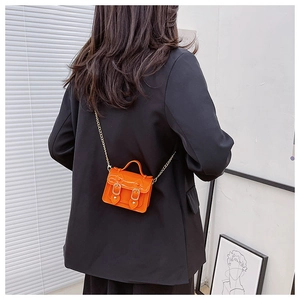 Close-up of vibrant orange jelly mini crossbody bag with gold chain strap on model