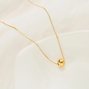 Minimalist gold ball pendant necklace with sleek snake chain shown on elegant white silk