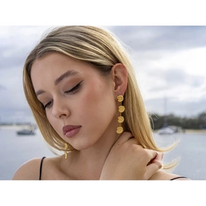 Close-up of long layered golden shell drop earrings worn by a model on a sunny beach