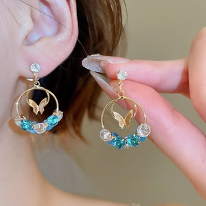Detail of gold butterfly earrings with blue and clear zircon stones on a model