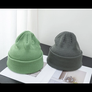 Berretti in maglia a coste verde e grigio scuro per uomo e donna su sfondo neutro