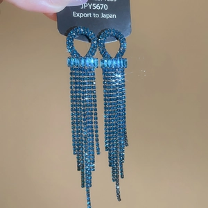 Detail showing blue tassel earrings with sparkling rhinestones on a black display card