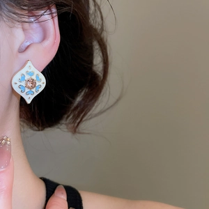 Close-up of diamond-studded diamond-shaped heart earring on model with vintage blue clover pattern
