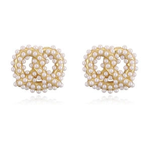 Detailed view of pretzel shaped gold earrings set with small white pearls on white background