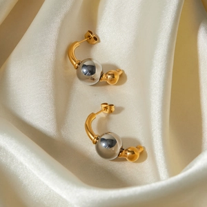Détail de boucles d'oreilles bicolores or et argent sur fond de tissu en soie blanche