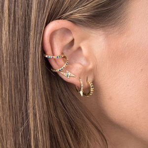 Macro shot of colorful zircon lightning stud earrings and gold ear cuffs set on ear