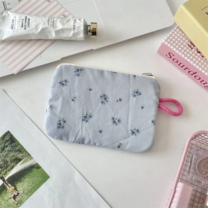 Close-up of light blue floral cotton makeup bag with pink lanyard on white desk