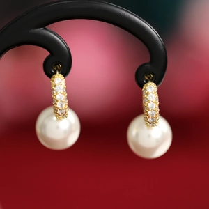 Close-up of pearl drop earrings with gold rhinestone hoops on black jewelry stand