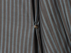 Détail macro d'une chemise en popeline marron à rayures bleu clair et bouton ambre en résine