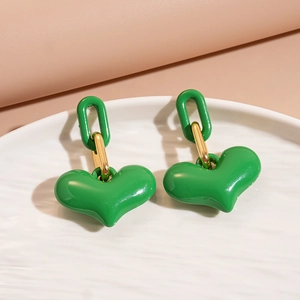 Close-up of bright green heart pendant earrings with gold metal links on a white tray