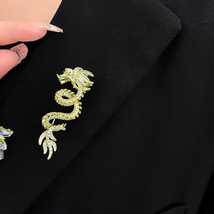 Detailed close-up of a gold-plated dragon brooch with sparkling crystals on a black blazer