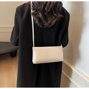 Detailed view of a white minimalist shoulder bag on a black coat in a clean studio setting
